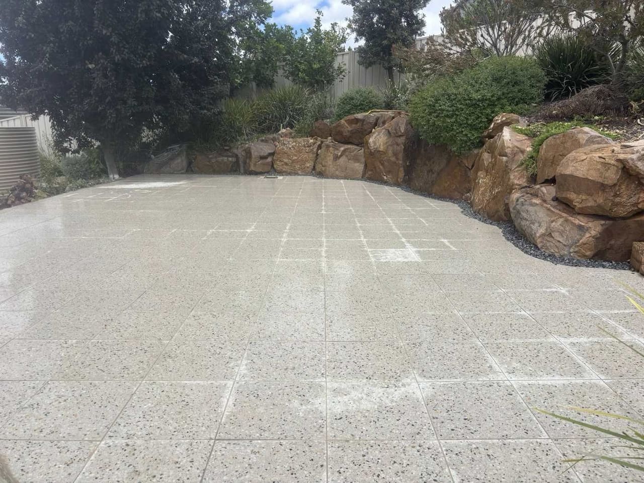 Granite patio with natural boulder retaining wall and garden landscaping — May Paving