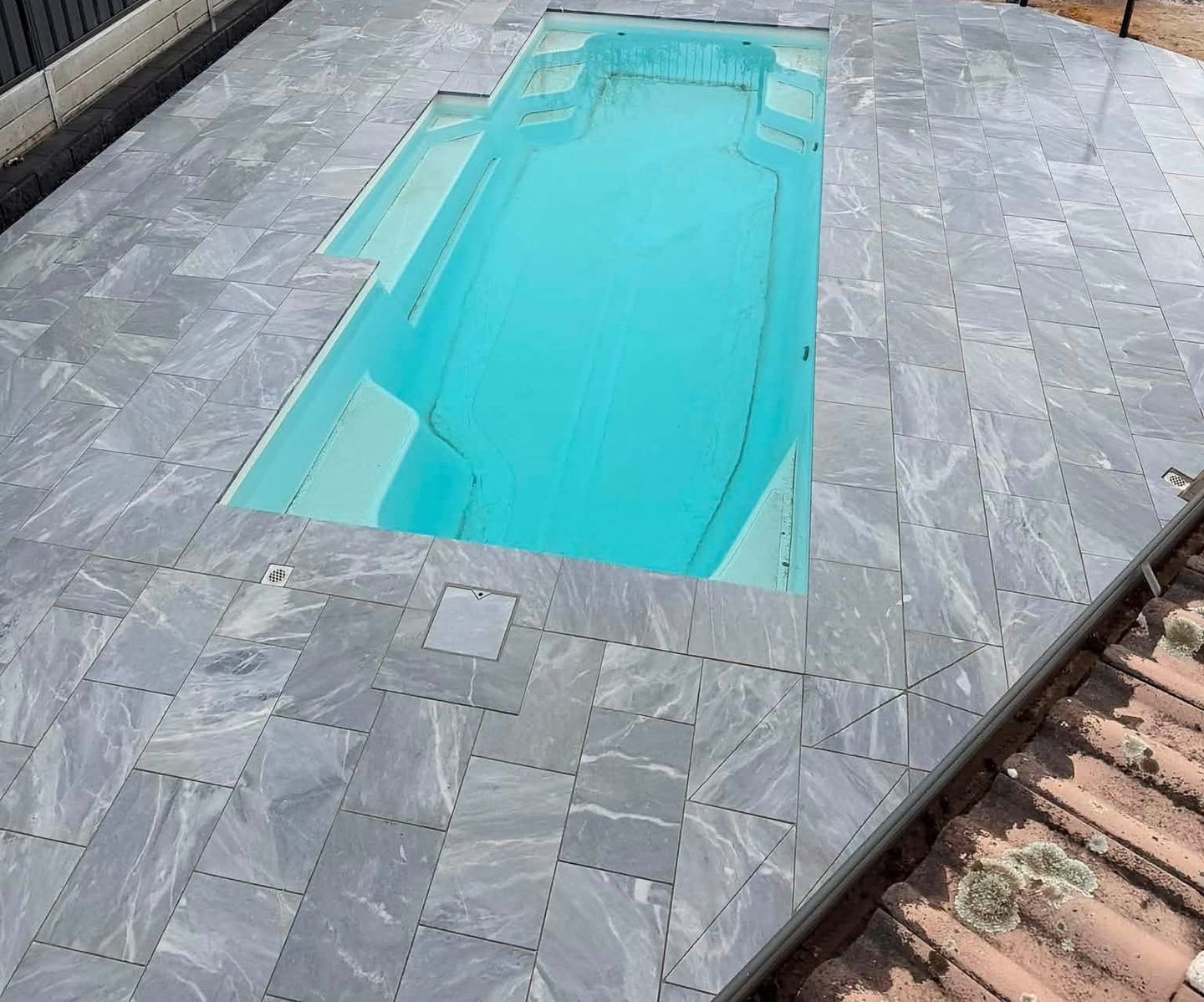 Marble-look pavers wrapping a bright blue fibreglass pool — May Paving