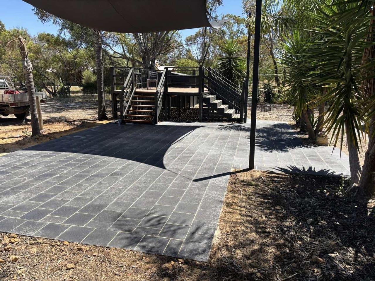 Wide dark slate patio under shade sail with composite deck and staircase — May Paving